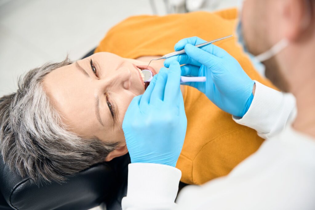 Dental practitioner using mouth mirror and dental probe to examine client teeth